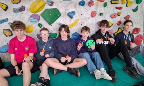 Students holding medals at the bottom of a rock-climbing wall